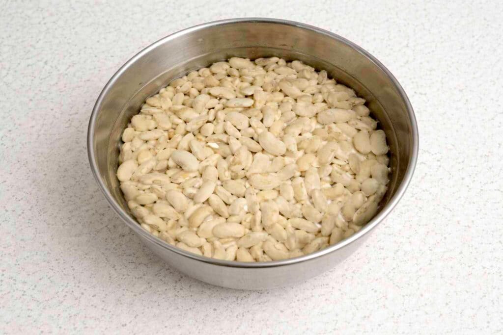 Alubias blancas cubiertas de agua en un bol de acero inoxidable, listas para el remojo