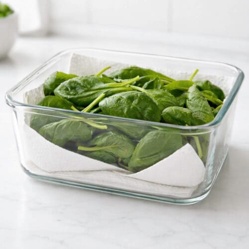 Hojas de espinacas frescas en un recipiente de cristal con papel de cocina para absorber la humedad y conservar la verdura más tiempo.
