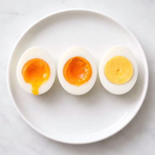 Tres huevos cocidos cortados por la mitad en un plato blanco mostrando diferentes puntos de cocción de la yema: líquida, melosa y firme.