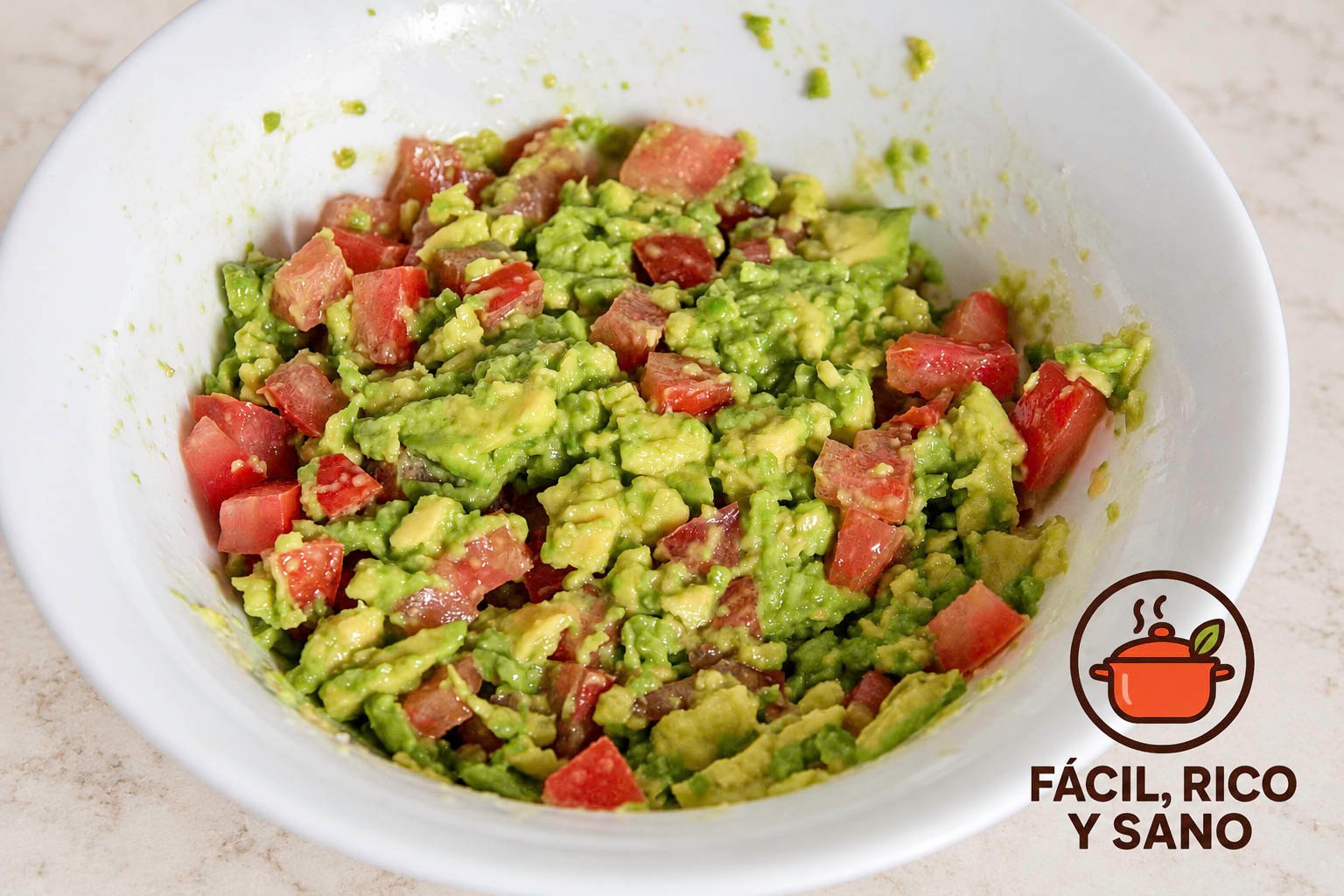 Aguacate machacado mezclado con tomate en dados y zumo de lima en un cuenco blanco