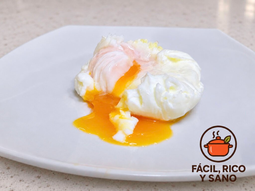 Huevo poché abierto sobre un plato blanco, con la yema líquida derramándose