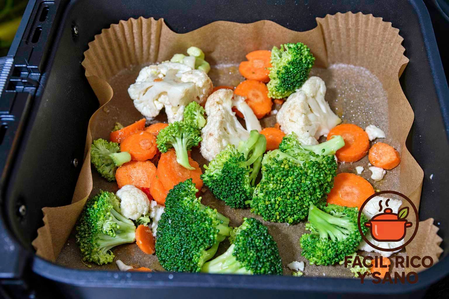 Brócoli, coliflor y zanahoria frescos con aceite de oliva en la cesta de la air fryer forrada con papel de horno, antes de asarlos